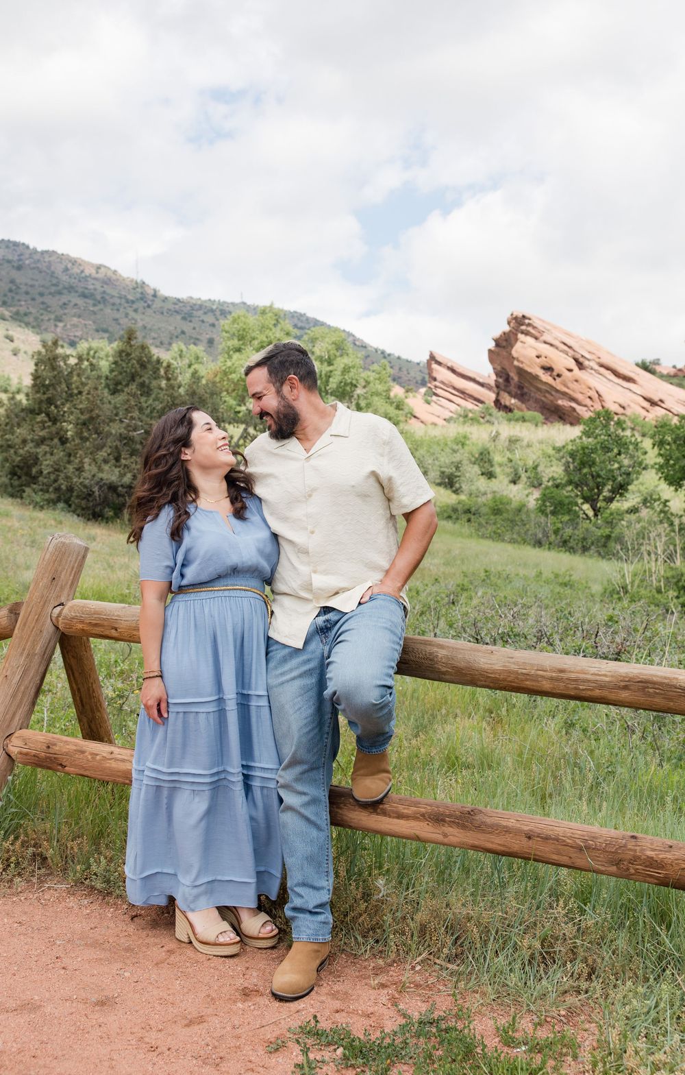 A couple shares a romantic moment while leaning against a wooden fence at Red Rocks Park.