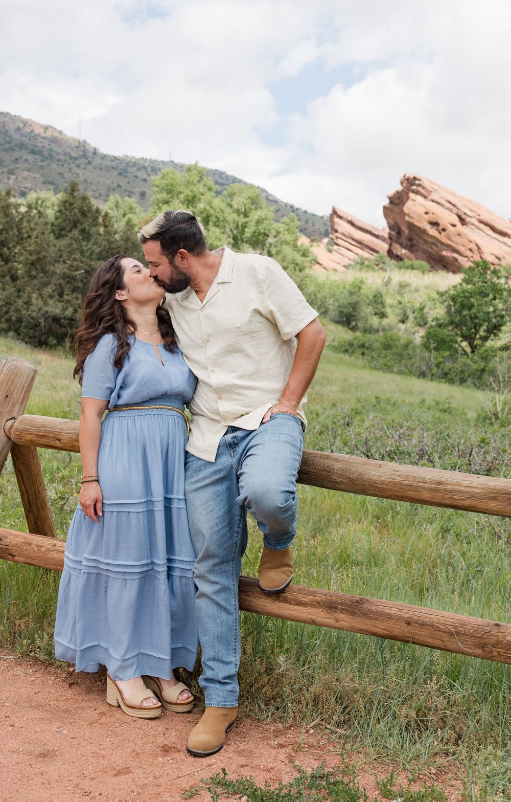 Couple shares romantic moments on a wooden fence with scenic red rocks and mountains in the background.