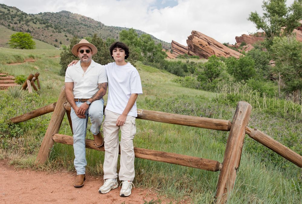 Two people pose by a wooden fence with Red Rocks formations visible in the background.