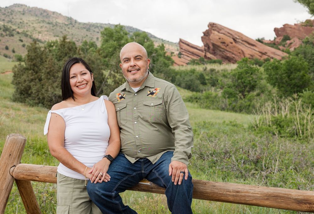 Loving couple poses together on wooden bench against scenic red rock formations at sunset.