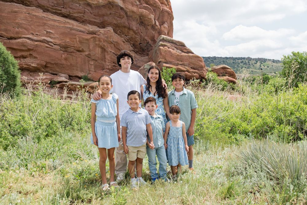 People stand together in coordinating blue outfits against dramatic red rock formations at a scenic outdoor location.