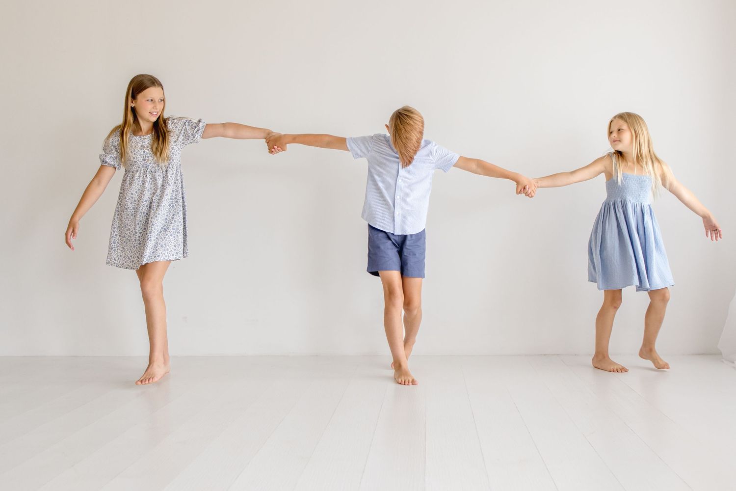 Kids in coordinating blue and white outfits dancing playfully in a minimalist white studio setting.