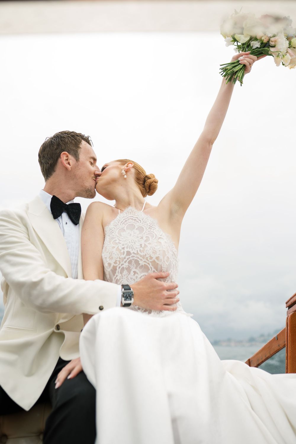 A romantic wedding moment captured in white attire with a bouquet raised triumphantly.