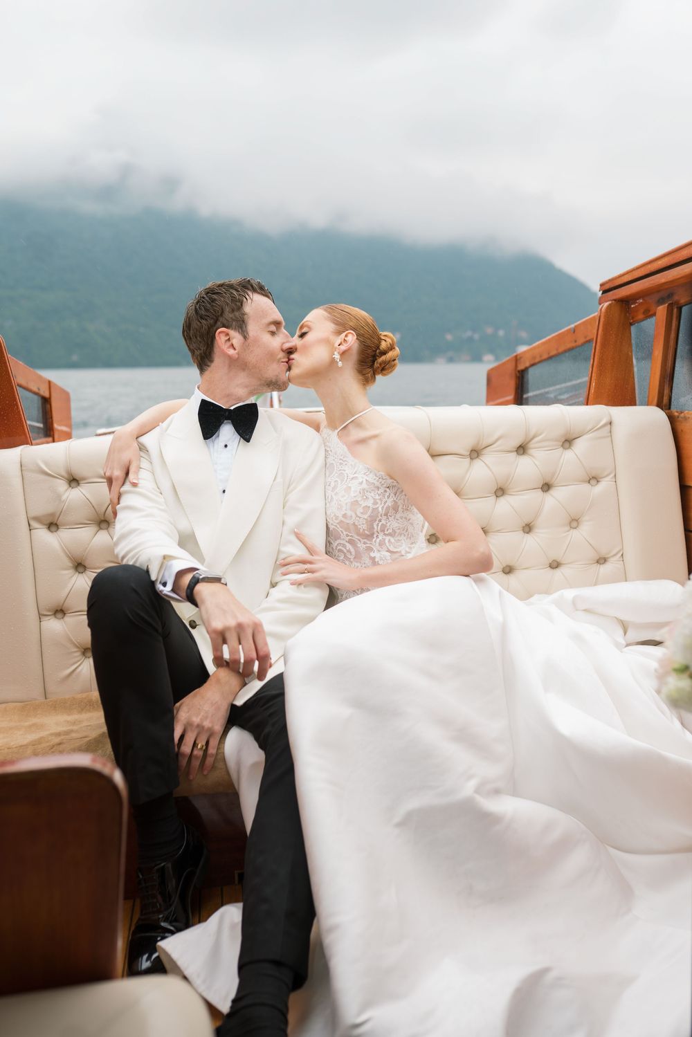 A elegant wedding couple reclines on cushioned seating aboard a classic wooden boat.