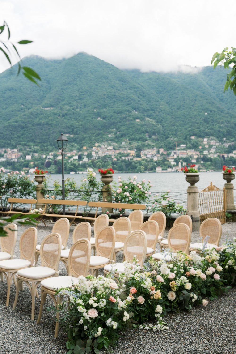 Lakeside wedding ceremony setup with white chairs and floral decorations overlooking mountain views.