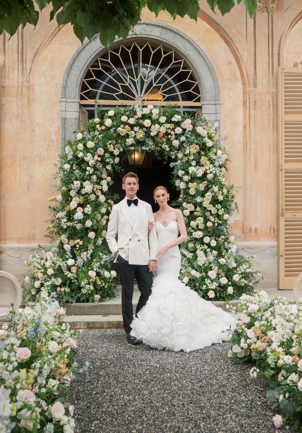 Elegant wedding ceremony setting with floral arches and white chairs in an Italian villa courtyard.