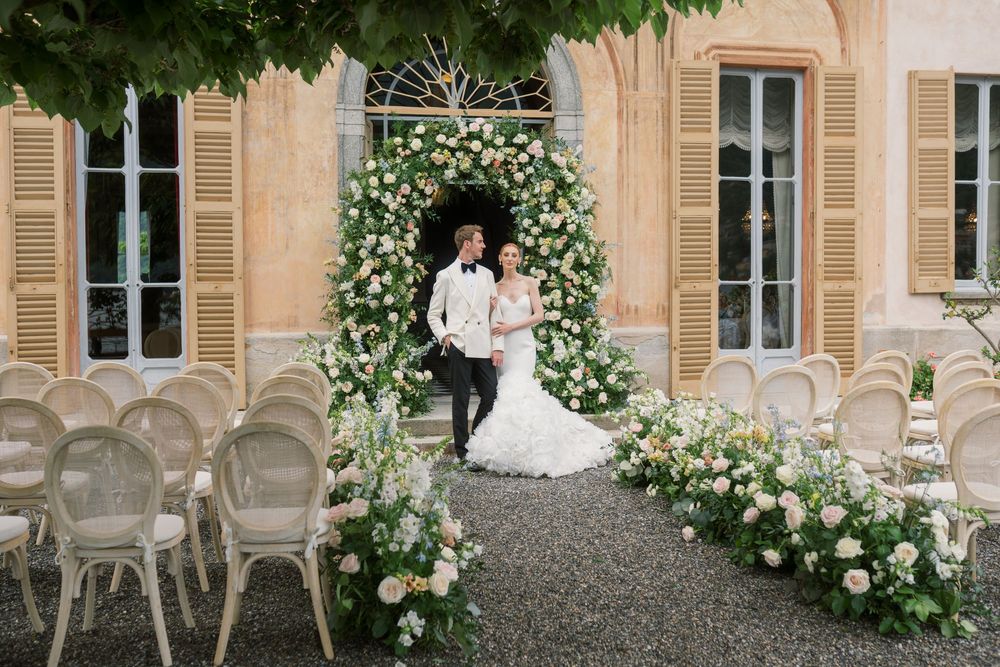 Wedding ceremony setup in villa courtyard with white chairs and rose-covered archways.