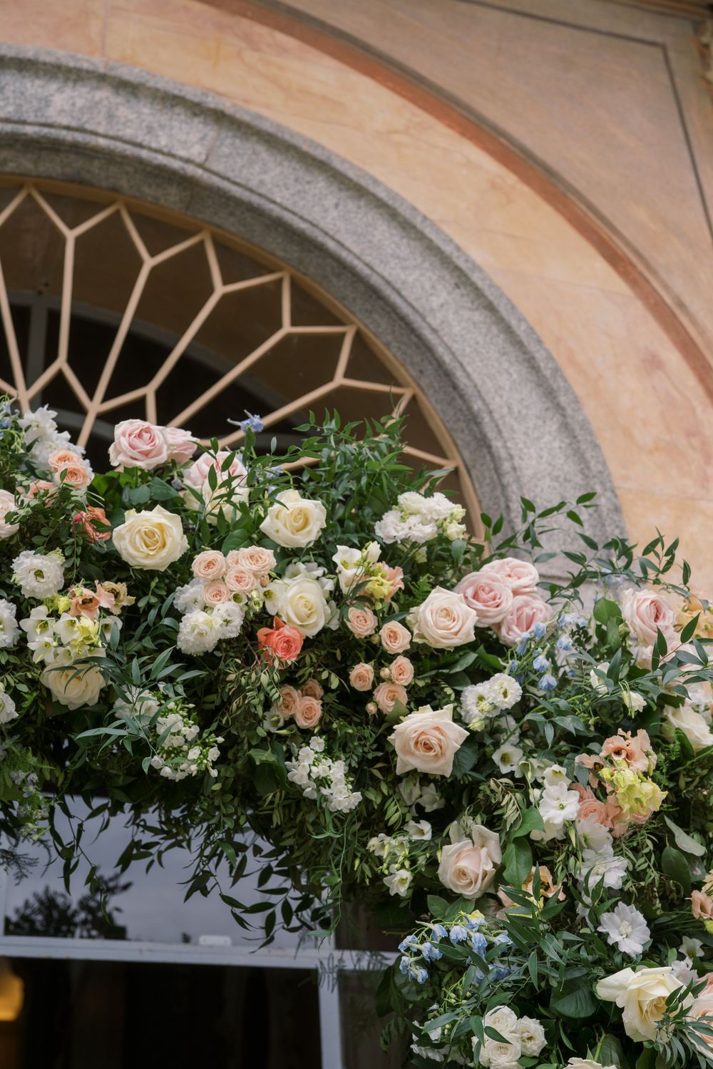 Delicate pink and white roses arranged in an arch above a historic Italian villa doorway.
