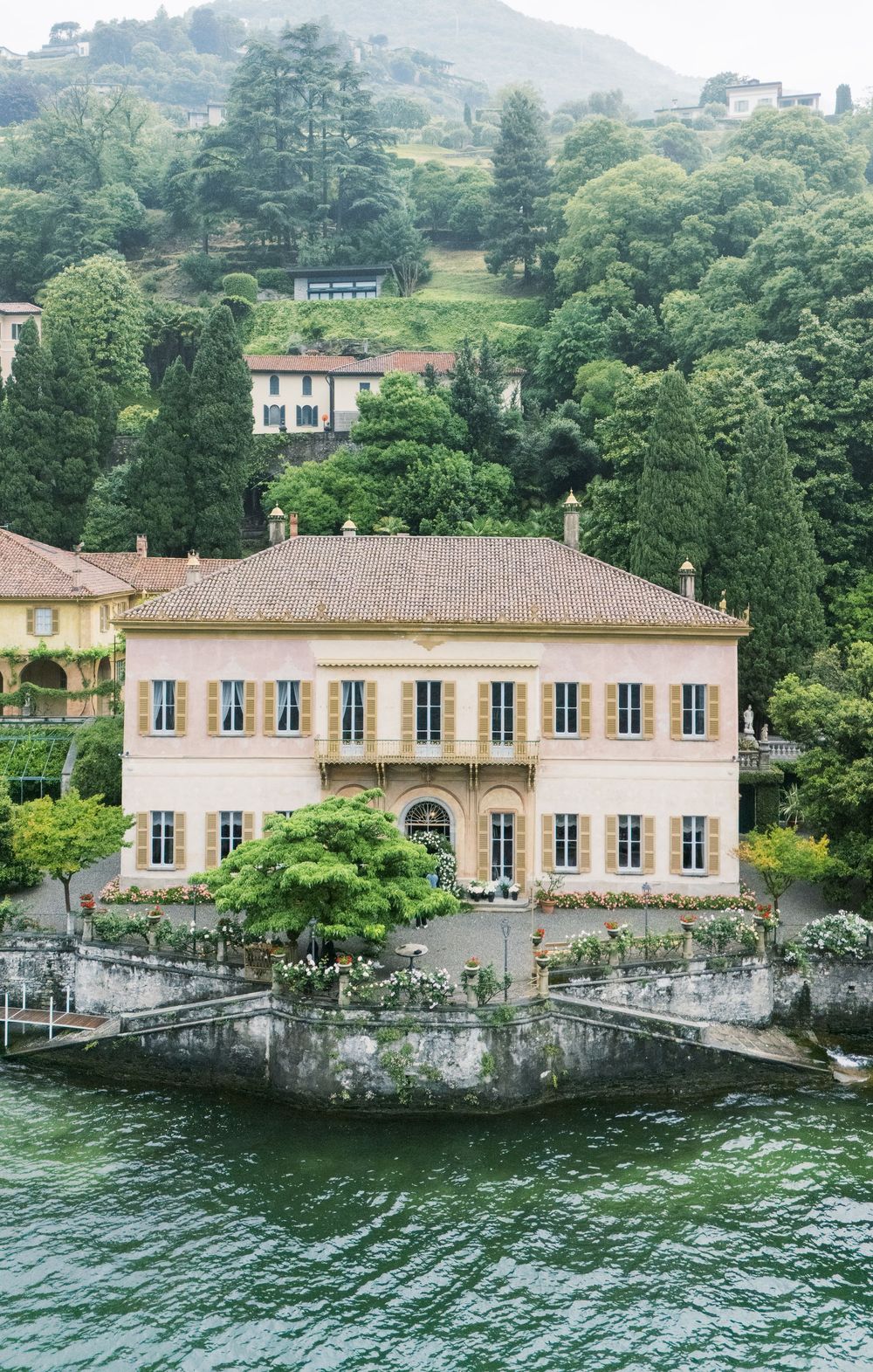 A stunning lakeside villa with yellow walls and large windows sits along the water's edge.