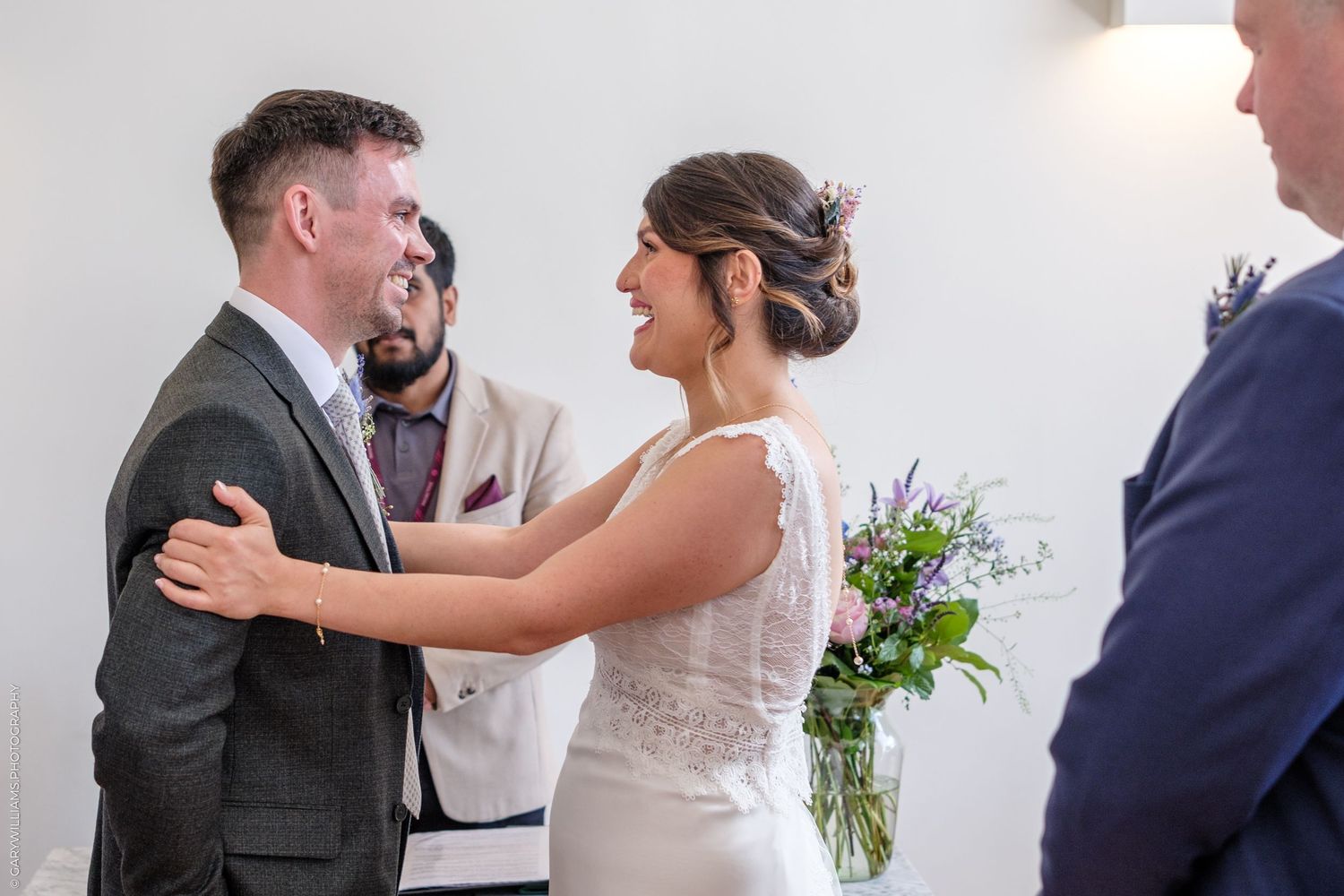 A tender moment is shared between a couple during their wedding ceremony with delicate purple florals in the background.