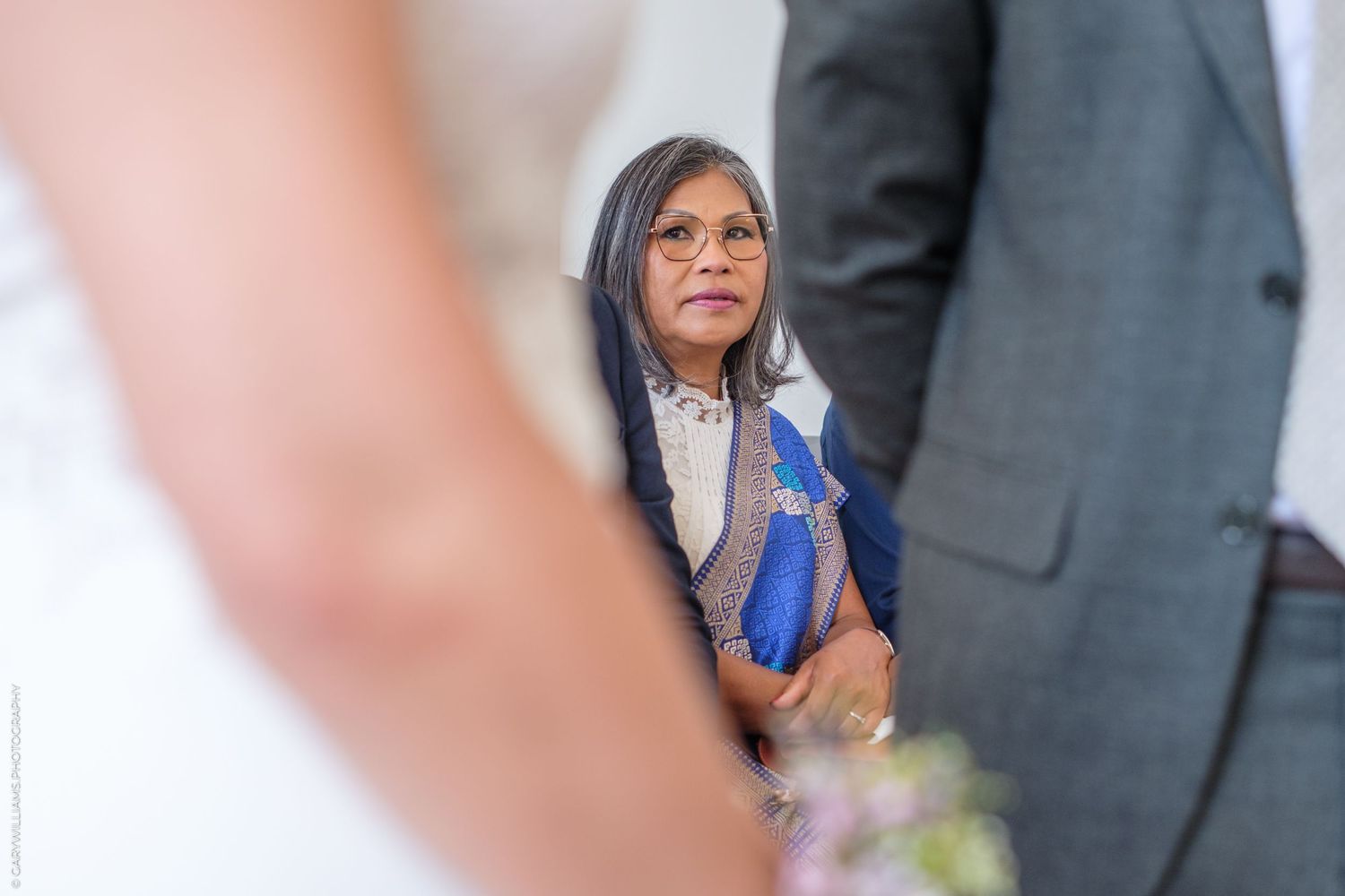 A person in business attire holding a blue ribbon stands between others at what appears to be a formal event.