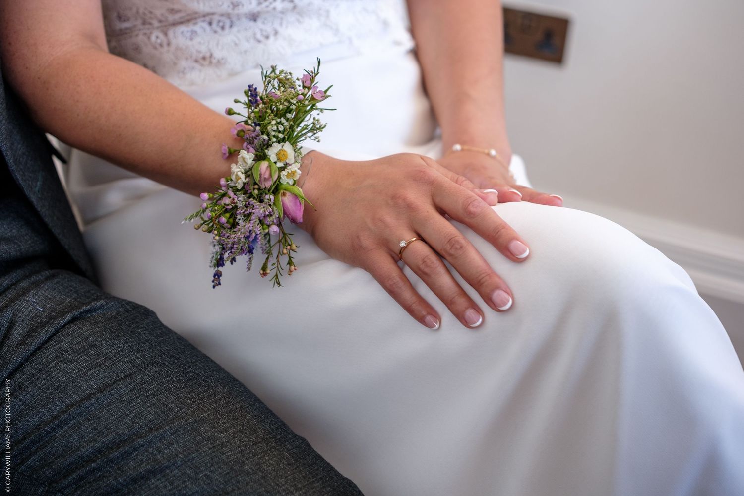 Close-up of a wedding couple's hands and formal attire with a small bouquet of delicate flowers.