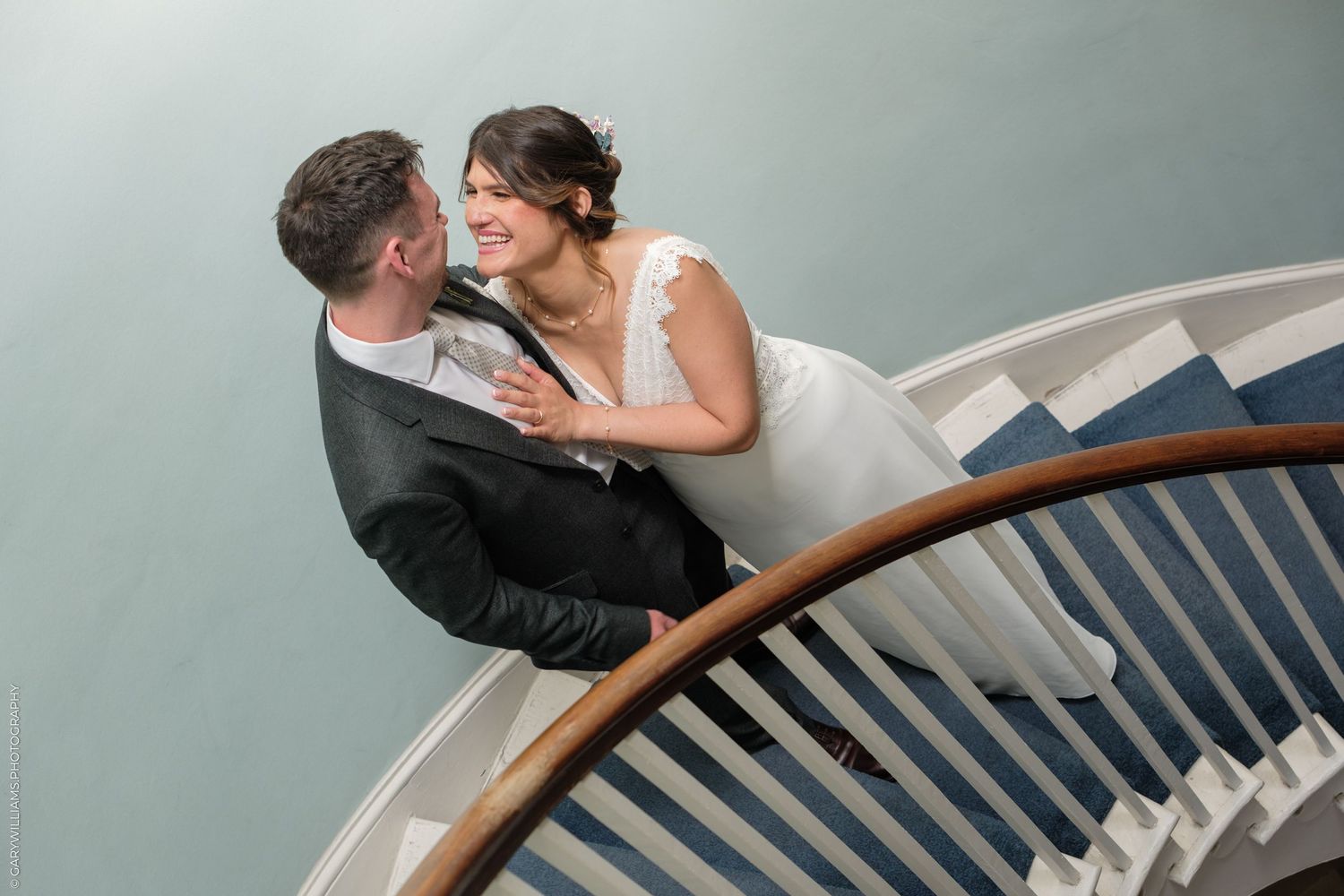Couple embraces while standing on spiral staircase, sharing romantic moments in elegant setting.