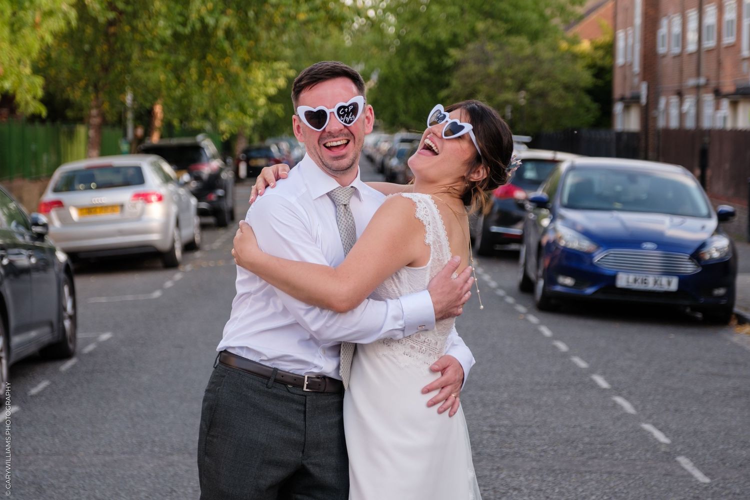 A joyful couple laughs together in the middle of a residential street on their wedding day.