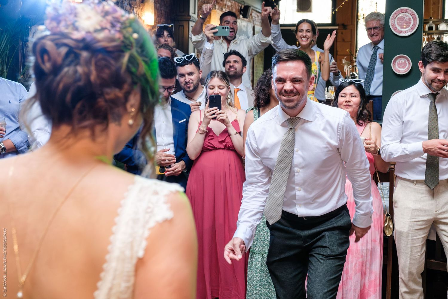 A joyful moment at a wedding reception as guests look on with phones capturing the celebration on the dance floor.