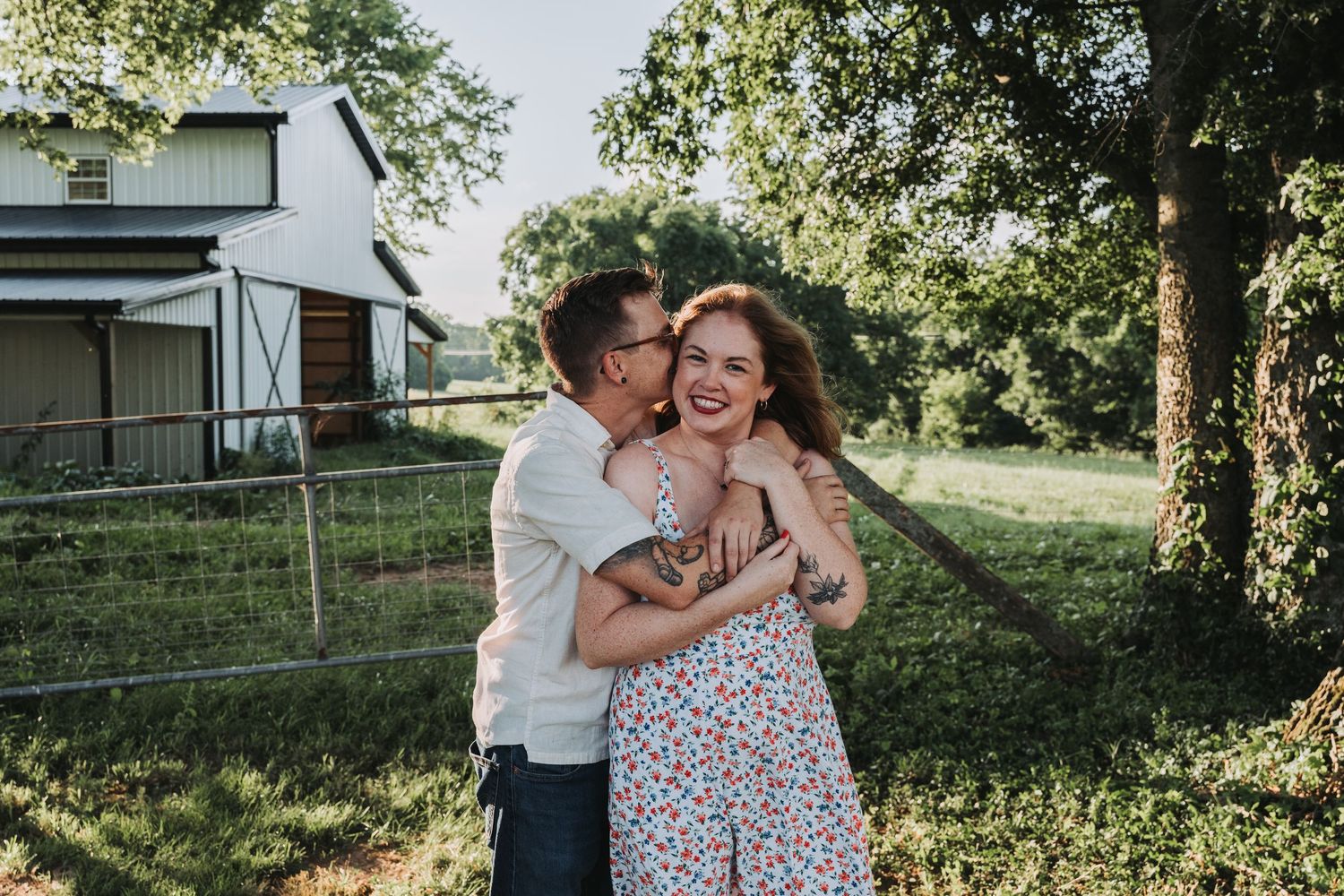 A couple shares a joyful moment together outdoors on a sunny day with trees and a house in the background.