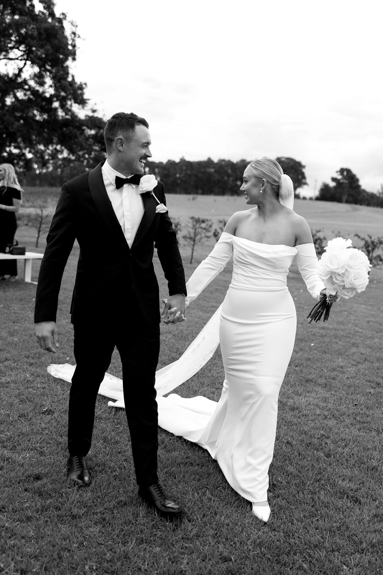 Black and white sequence of a couple on their wedding day playfully walking and posing together in a grassy field.
