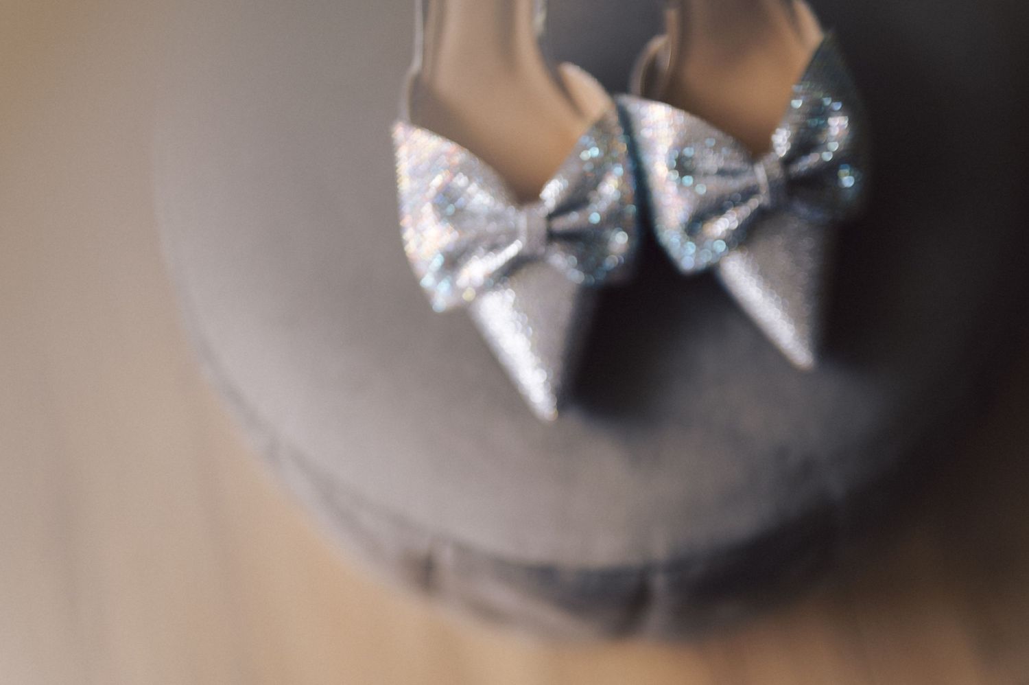 A pair of elegant silver pointed toe heels with bows sits on a gray surface in soft focus.