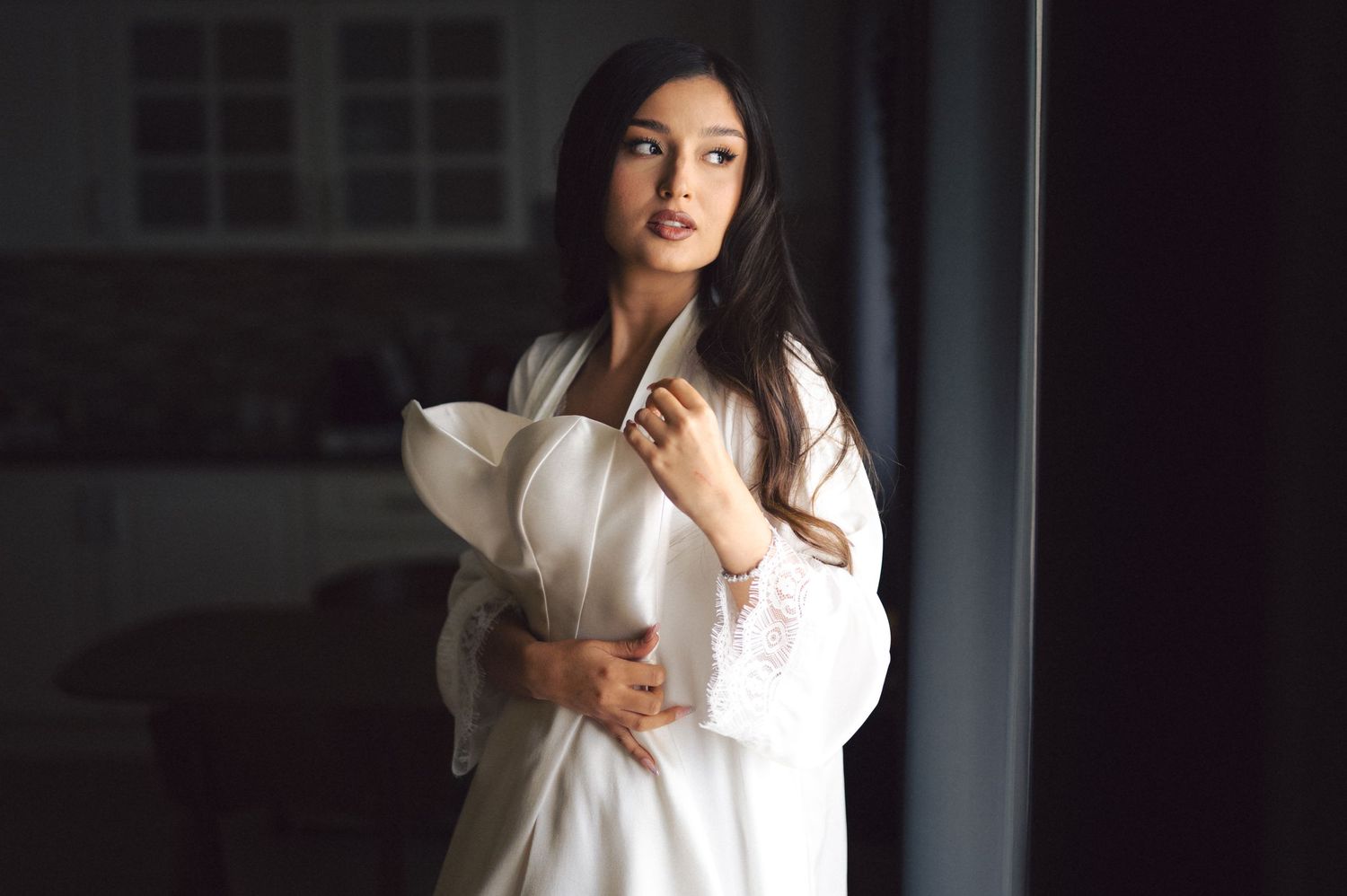 Woman in white poses gracefully in soft natural light against dark background.