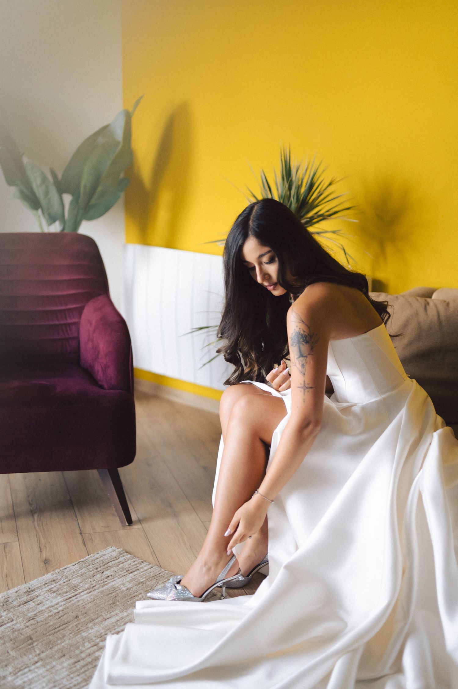 A sequence of photos shows someone in a flowing white dress leaning down to adjust their black heels against a yellow wall.