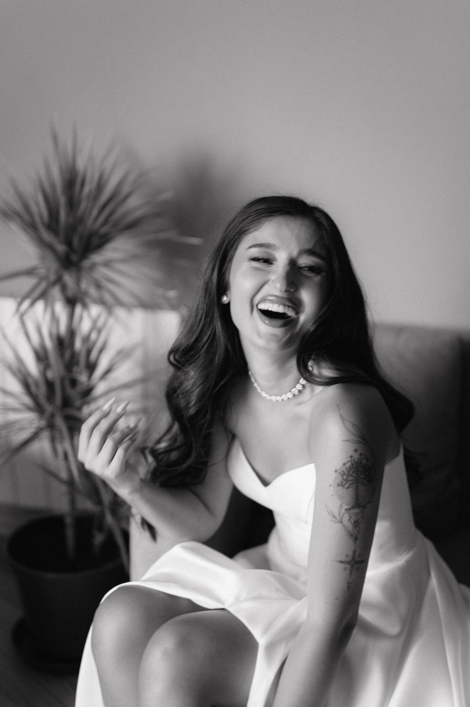 A joyful moment captured in black and white showing someone laughing while wearing a white dress and pearl necklace.