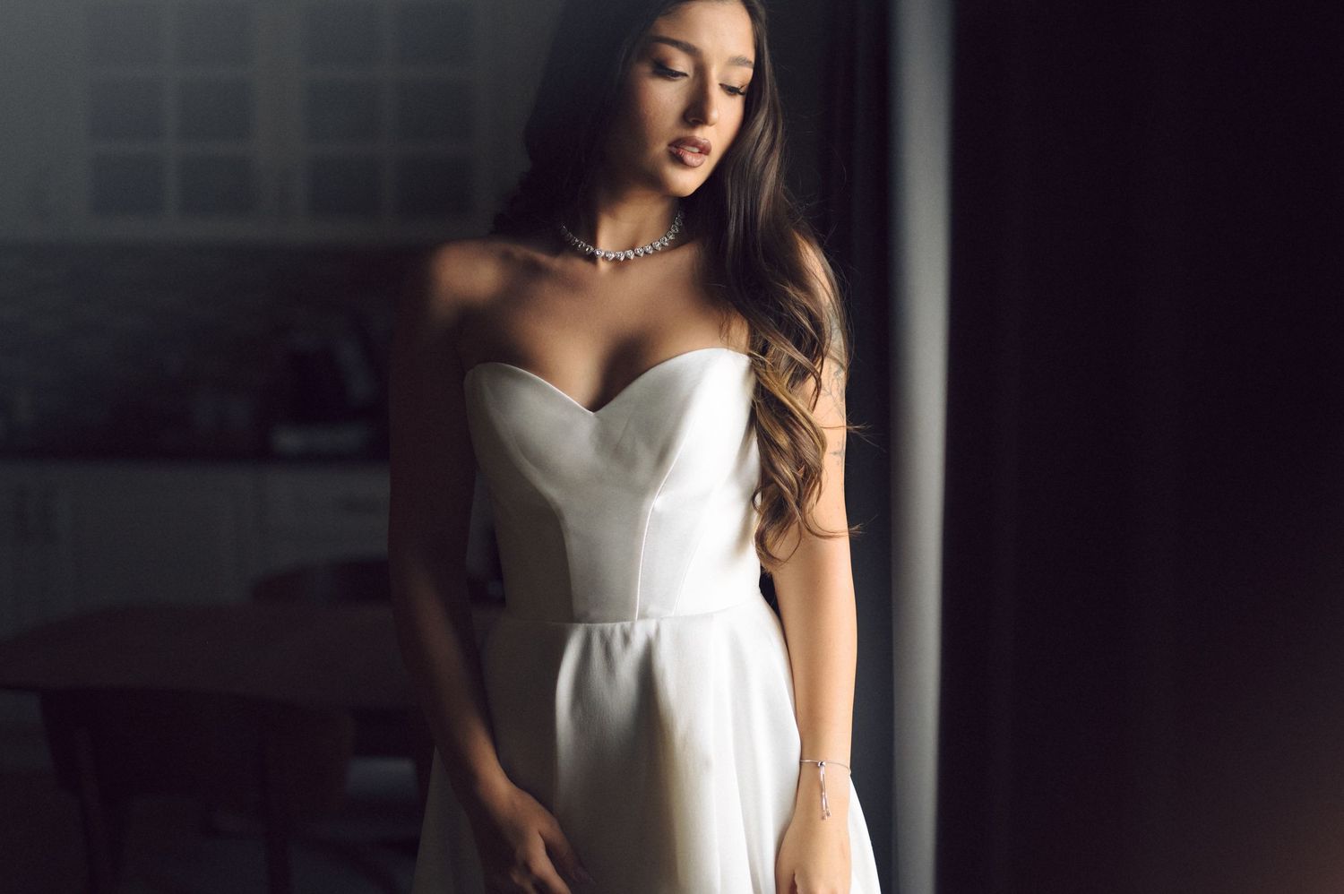 A woman in an elegant white strapless wedding dress stands in a softly lit room.