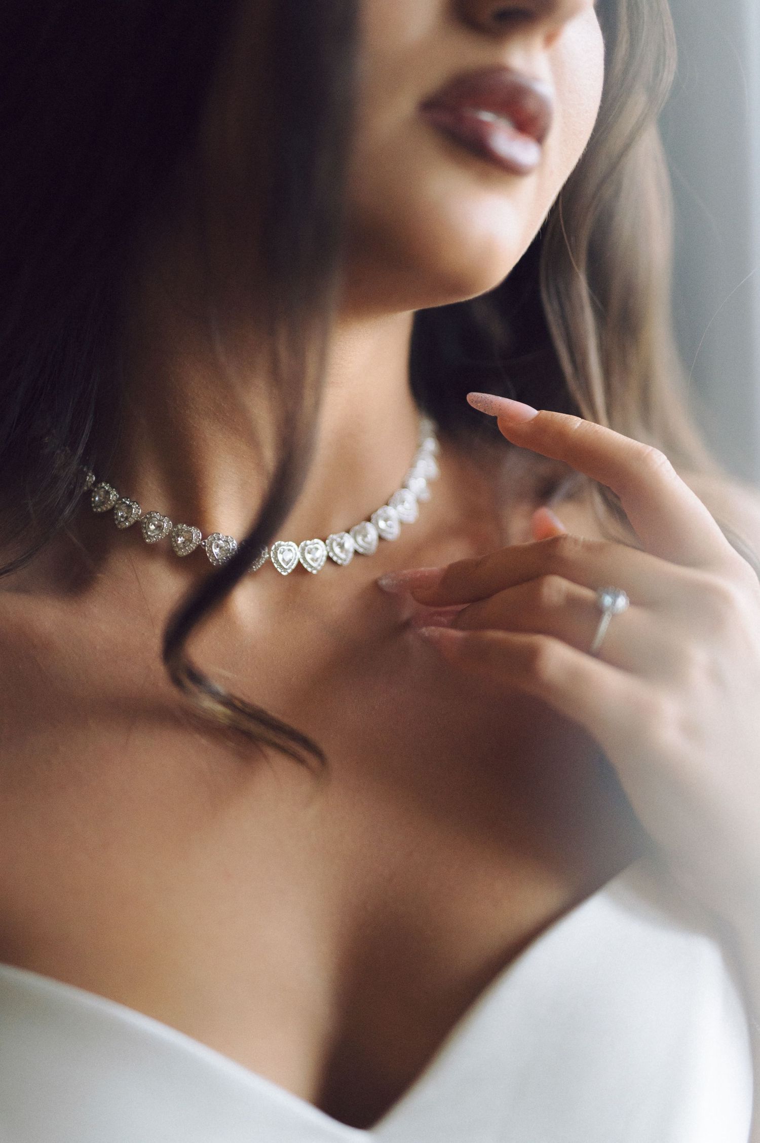 Elegant diamond necklace and ring sparkle against white fabric as delicate fingers touch the collarbone.