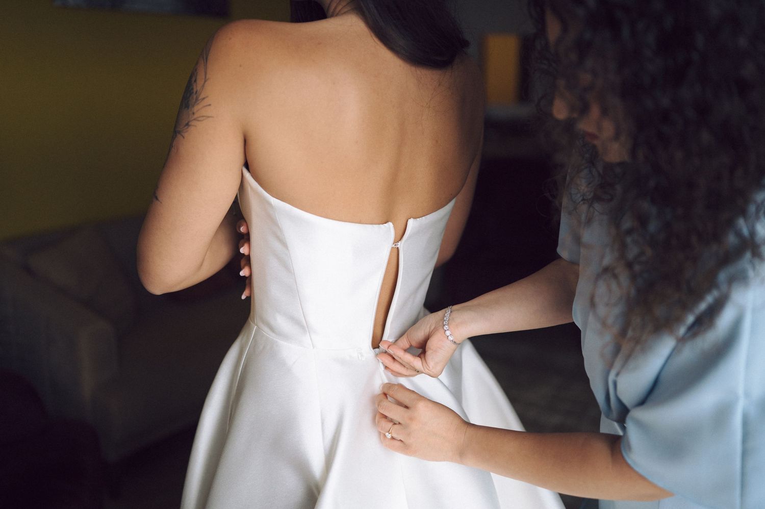 A person helps zip up a classic white wedding dress during bridal preparations.