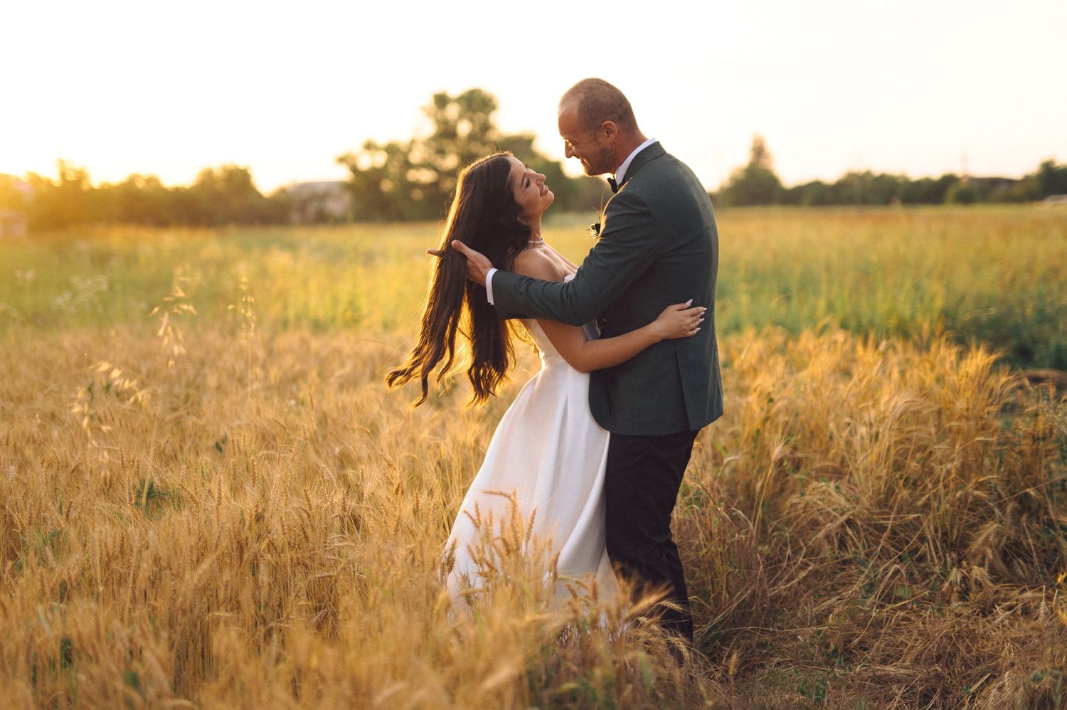 A couple embraces in a sunlit golden wheat field during sunset creating a romantic silhouette against the warm sky.
