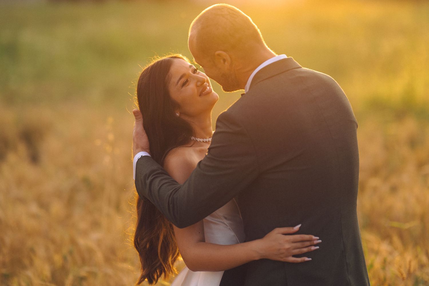 Sun-drenched couple shares intimate moment in field during golden hour portrait session.
