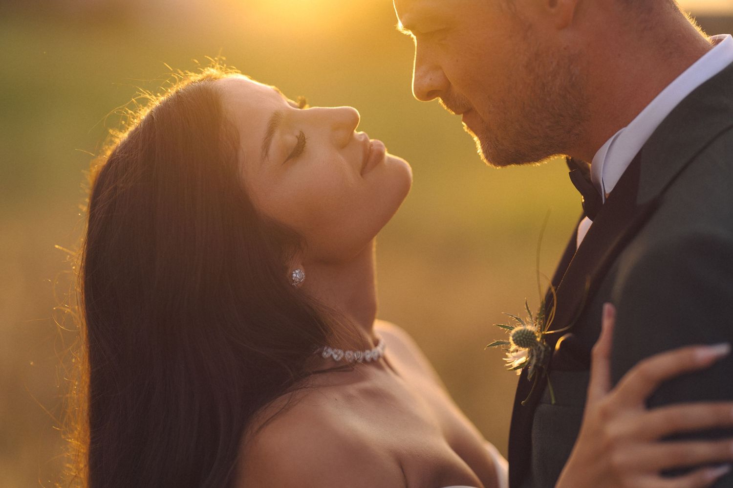 A romantic golden hour portrait of a couple embracing outdoors with soft sunlight creating a warm backlit glow.