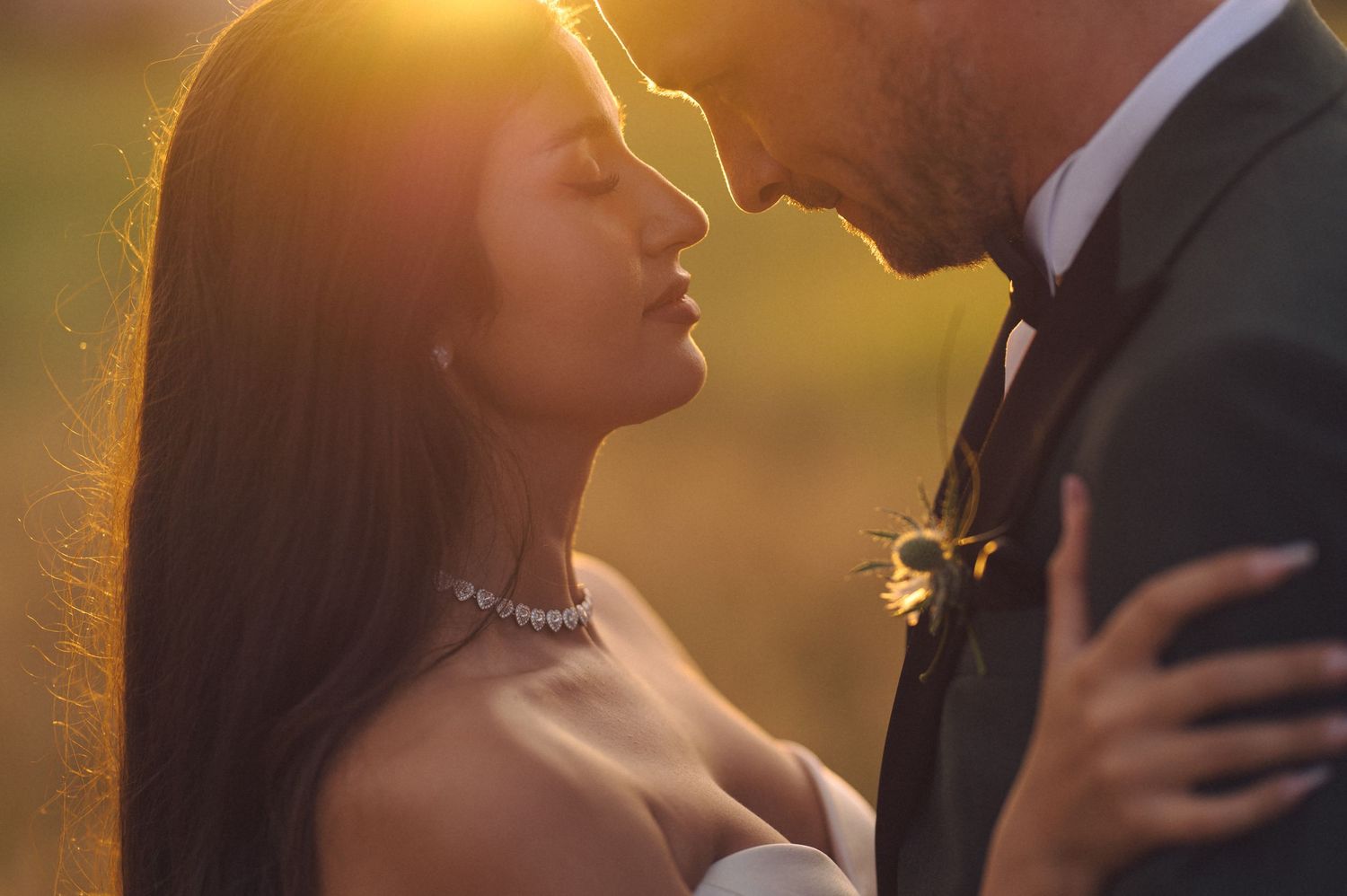 A couple embraces in golden sunlight during a romantic outdoor photo session at sunset.