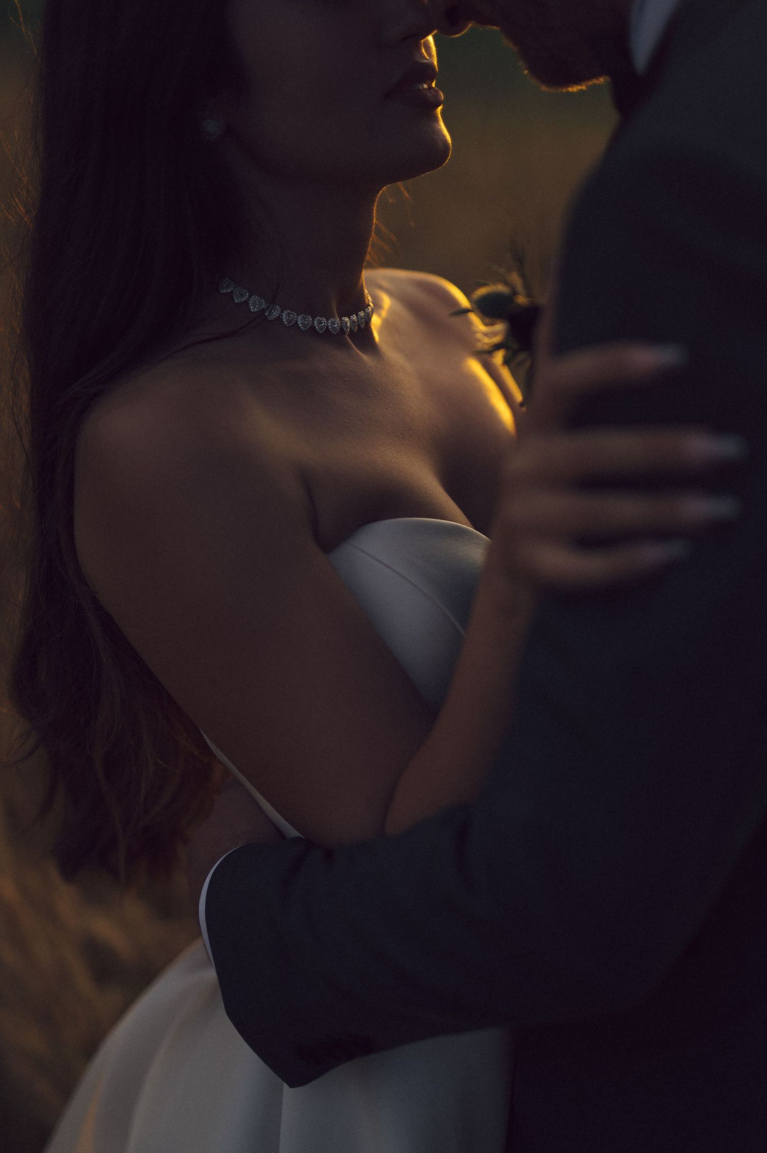A silhouetted figure in a dress stands in dramatic lighting with sunlight creating a warm glow around their neck.