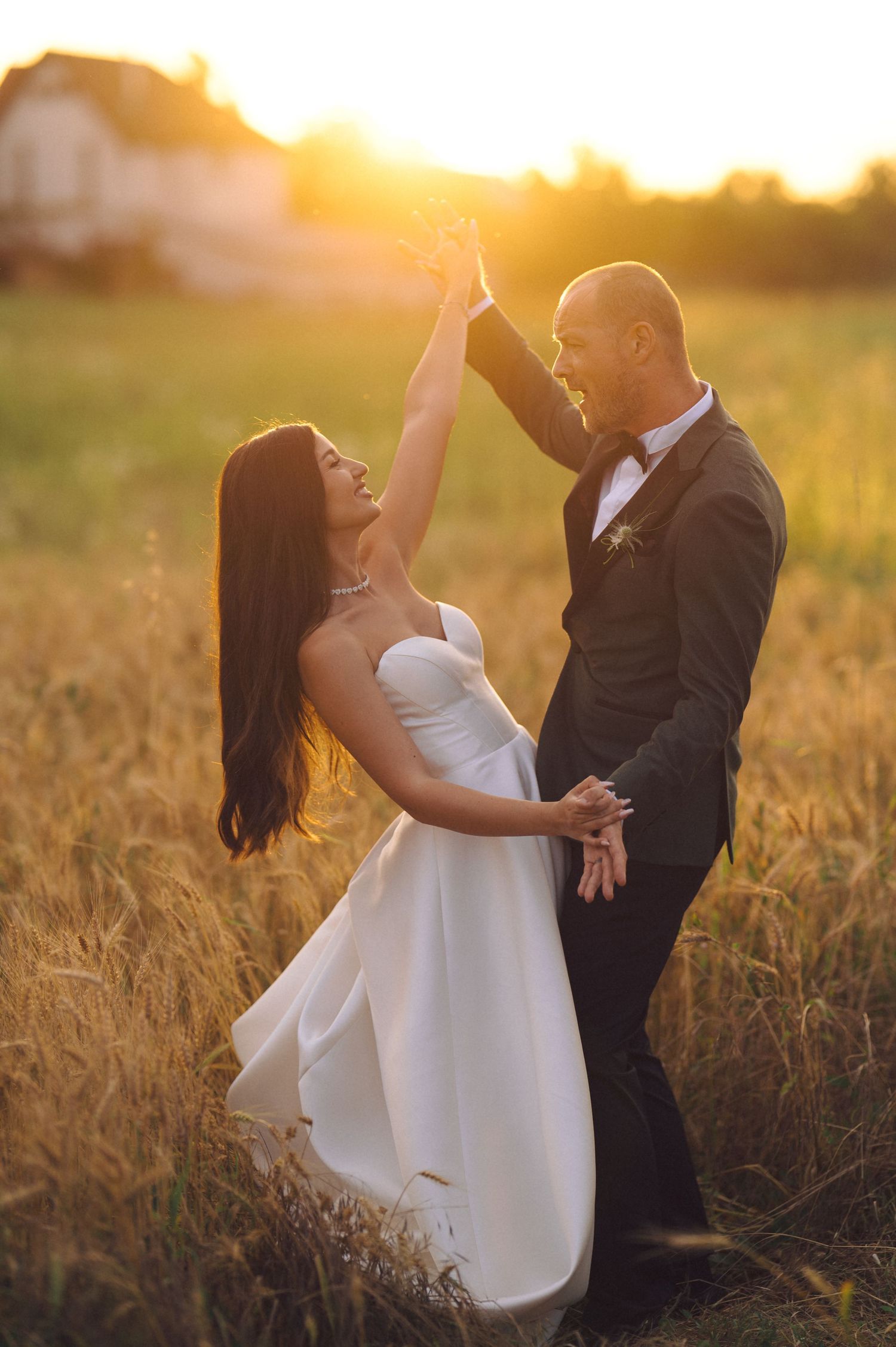 A couple dancing together in a golden wheat field at sunset, creating romantic silhouettes against the warm sky.