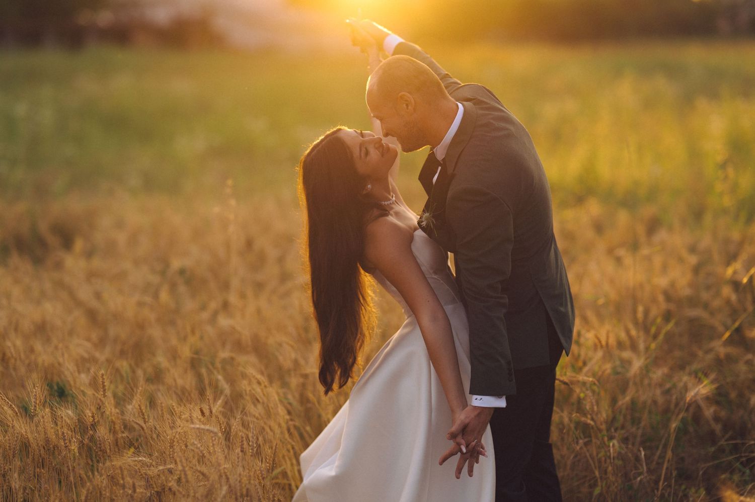 Intimate wedding portrait of a couple sharing a tender moment in a sunlit field of wheat.