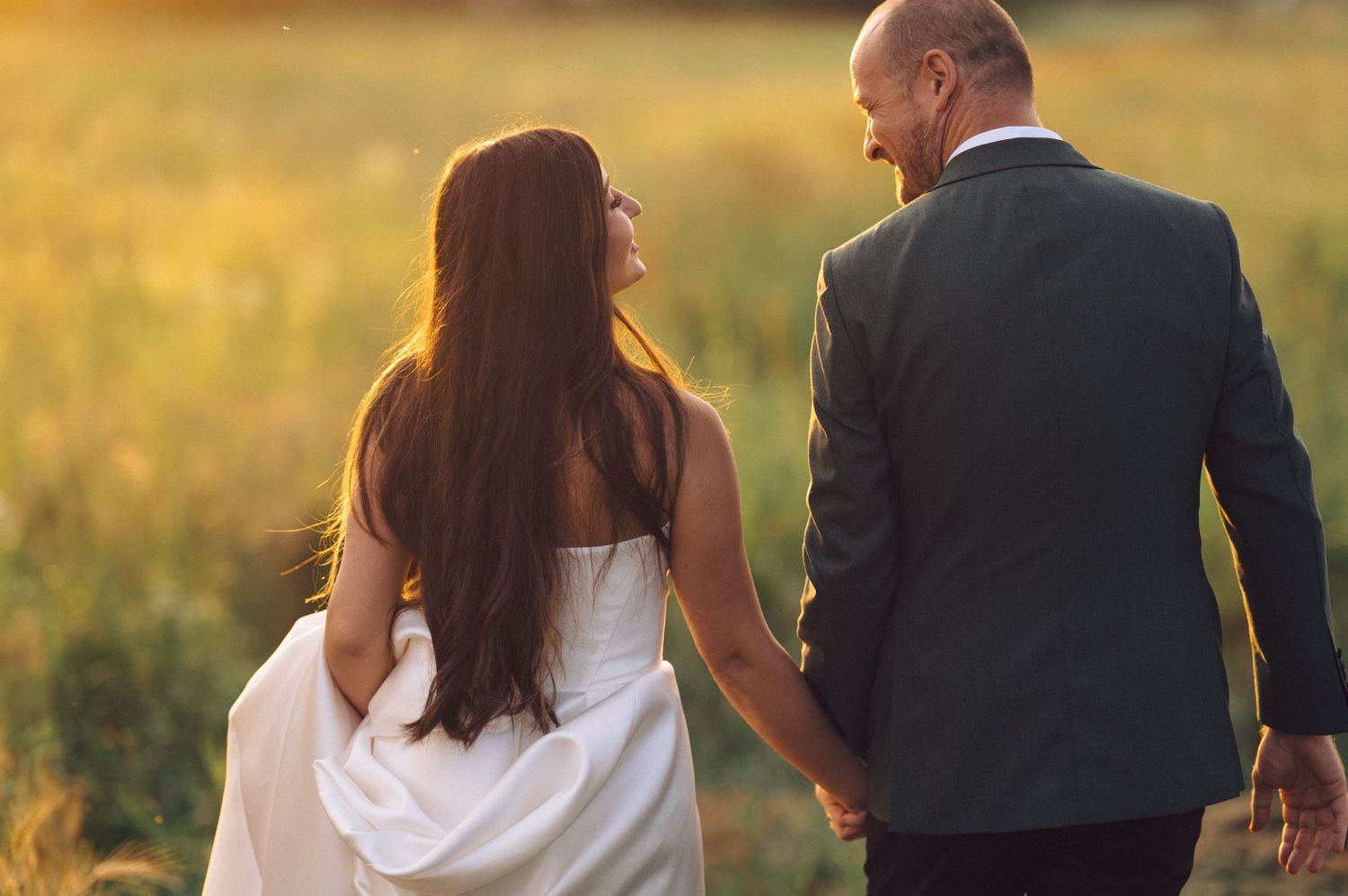 Couple walking through golden wheat field at sunset during romantic outdoor photoshoot.