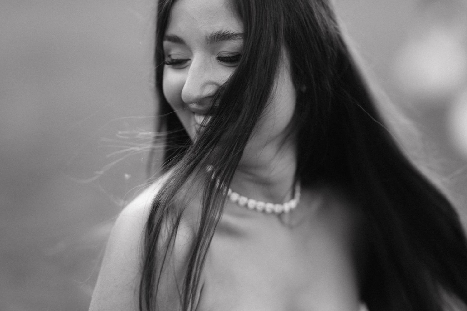Black and white portrait of woman with long dark hair wearing pearl necklace in soft focus.