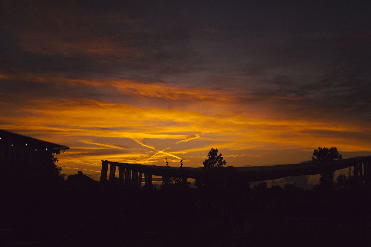 Dramatic orange and yellow sunset sky silhouettes buildings and structures against a dark landscape.