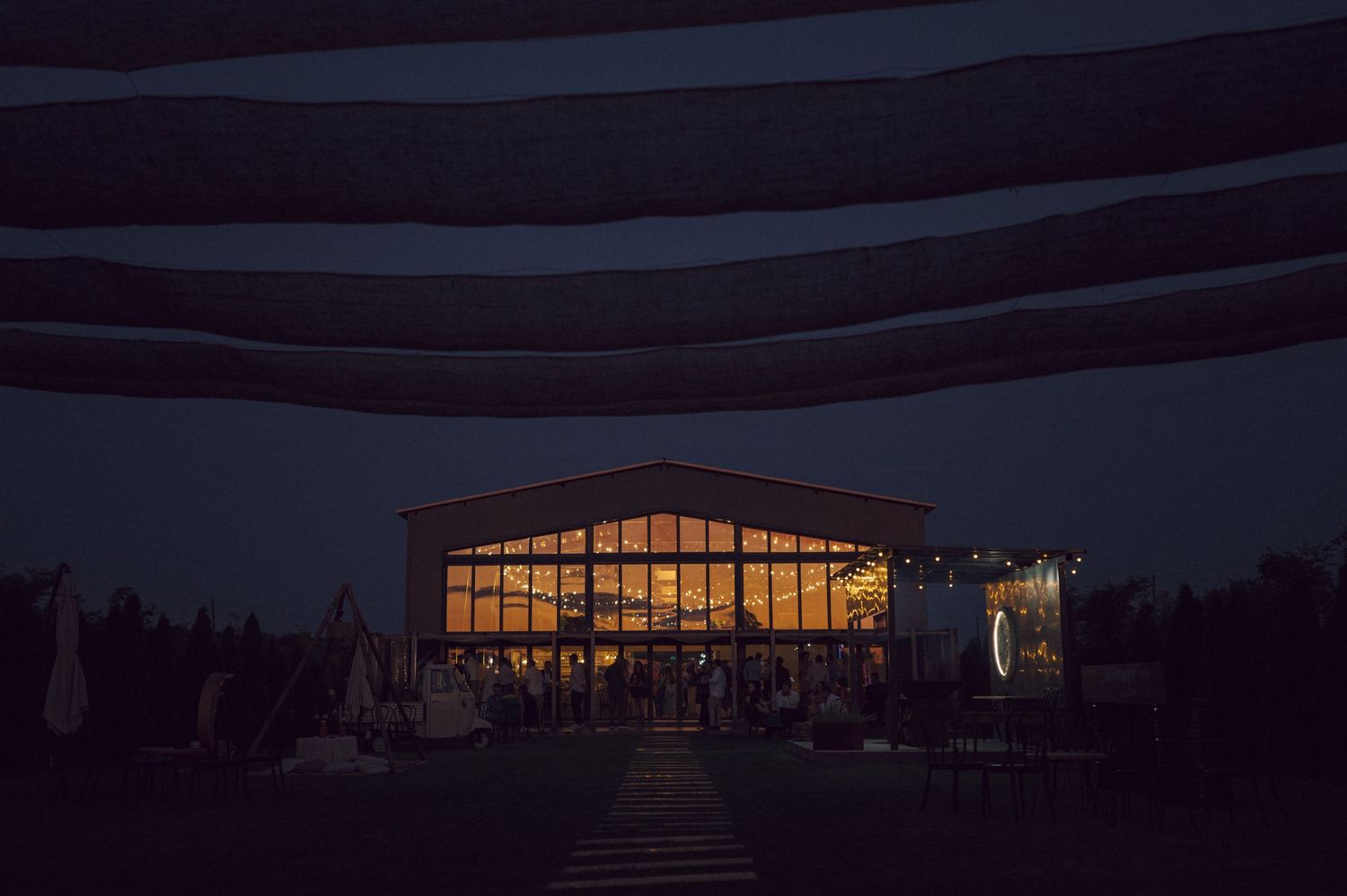 Illuminated barn venue glows warmly at dusk with large windows creating an inviting atmosphere.