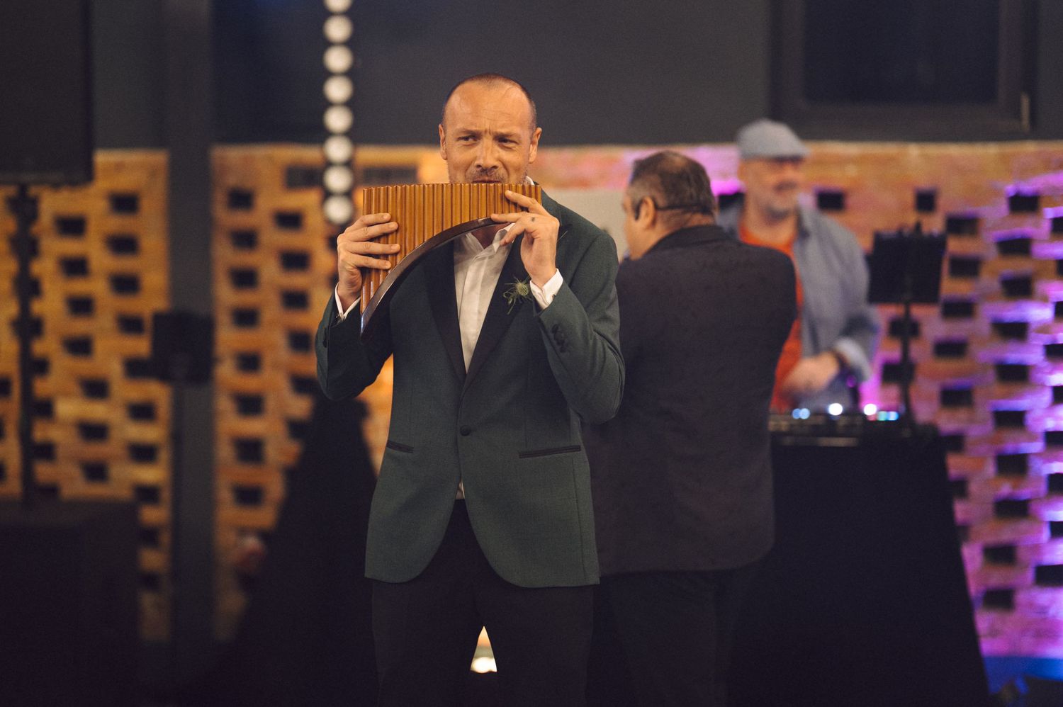 Man in suit jacket performing on stage with theatrical lighting and wooden decor.
