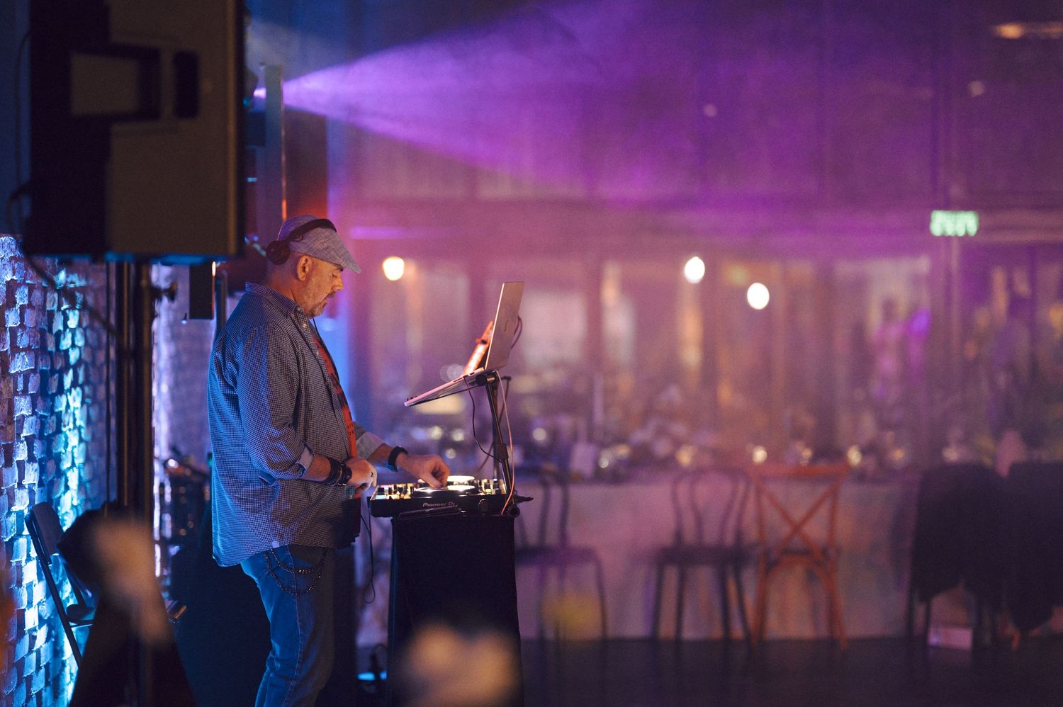 DJ performing at event venue with purple lighting and hazy atmosphere.