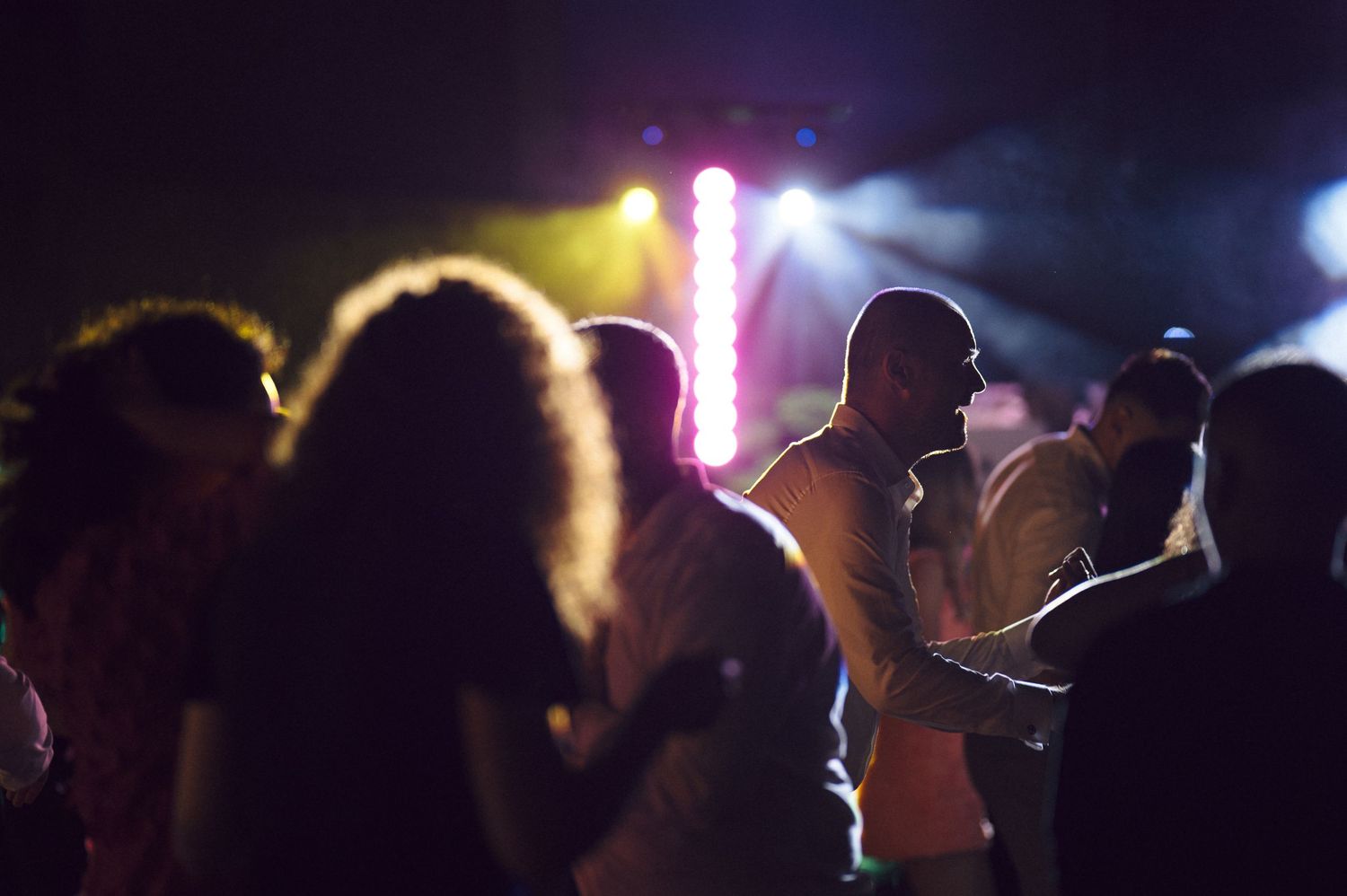 Silhouettes of people dancing at a party with colorful stage lights in the background.