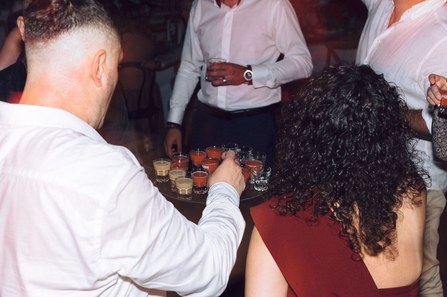 People in white shirts gathered around a table with appetizers or small plates at a social event.