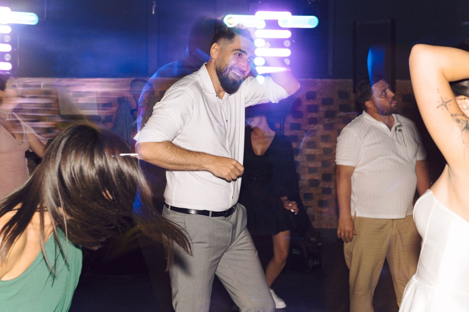 People dancing and enjoying themselves at a party with neon lighting and a brick wall backdrop.