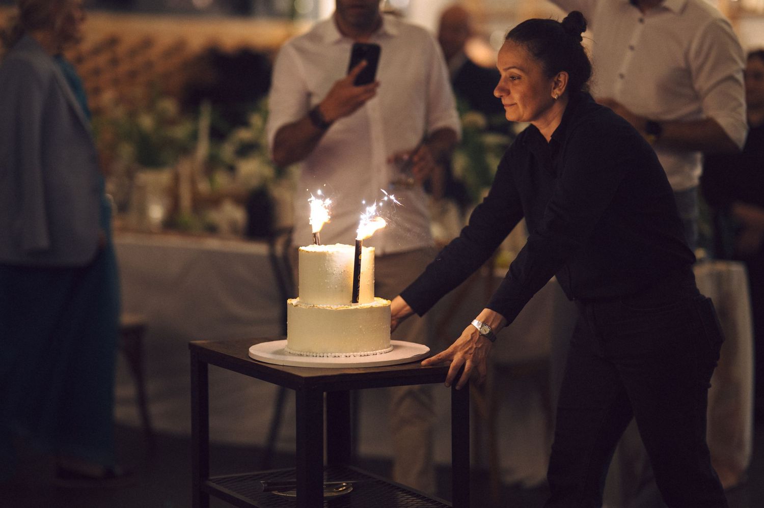Sparkler candles illuminate a birthday cake on a dark table during an evening celebration.