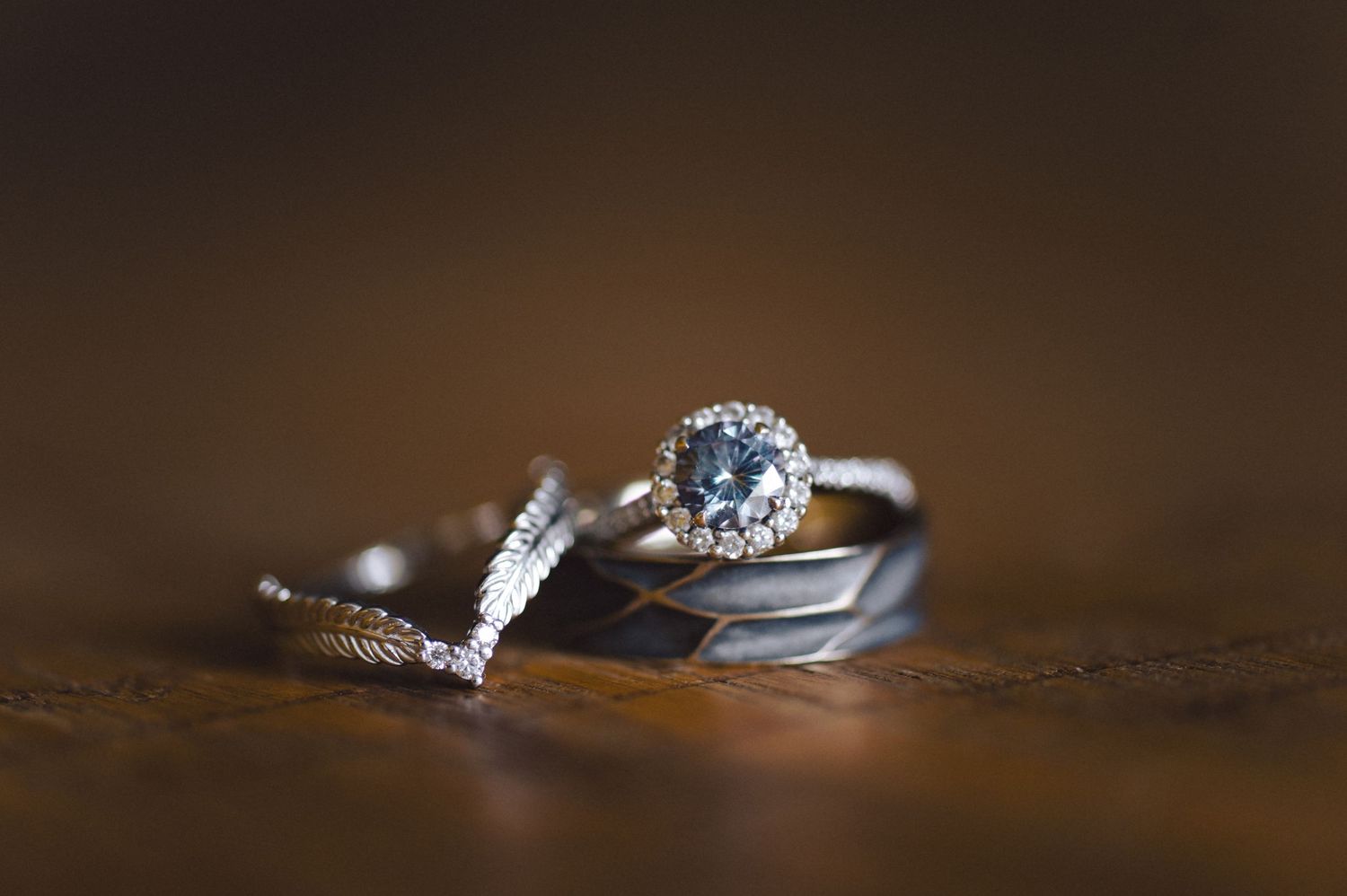 Two elegant silver wedding rings with diamonds displayed on a dark wooden surface in soft lighting.