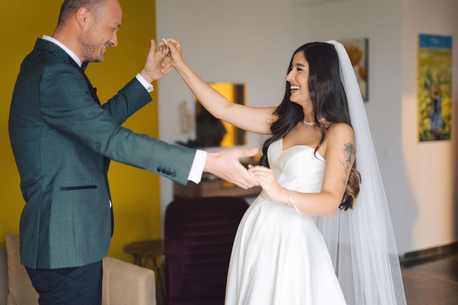 A couple in formal wedding attire dances together in a room with yellow walls.