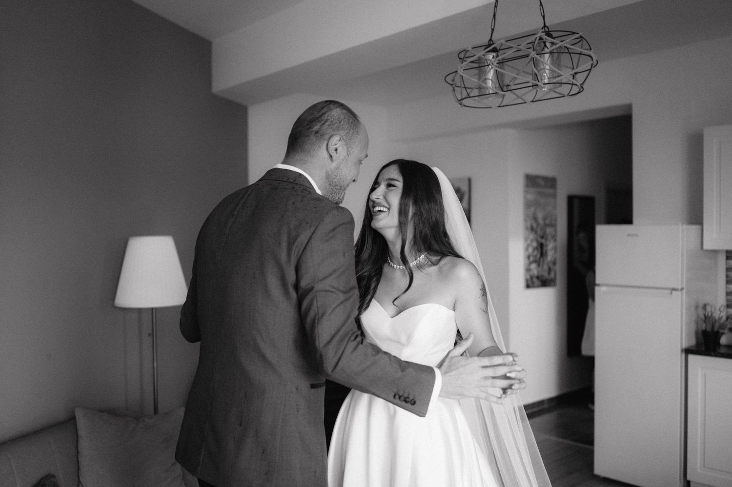 A tender black and white moment between a bride and groom in a room with elegant lighting.