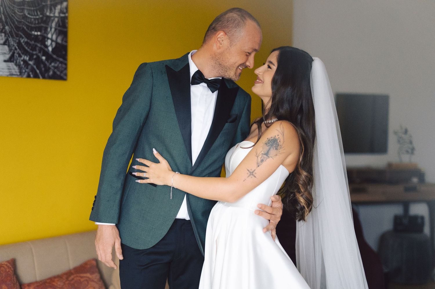 Newlywed couple shares romantic first dance moments in front of yellow wall at wedding reception.