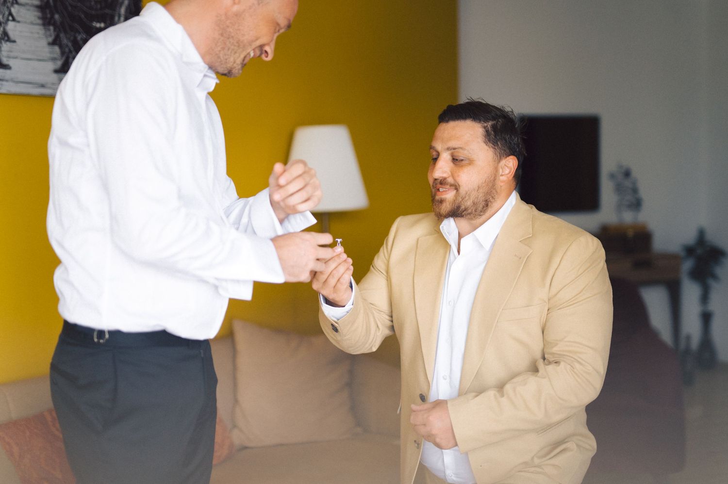 Two people in a business setting engage in conversation, one wearing a white shirt and another in a tan suit.